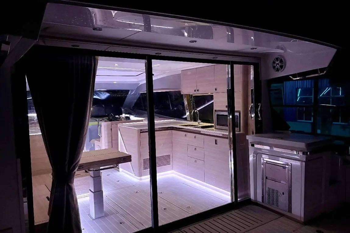 Modern yacht interior featuring a stylish kitchenette, illuminated under-cabinet lighting, and elegant sliding glass doors.